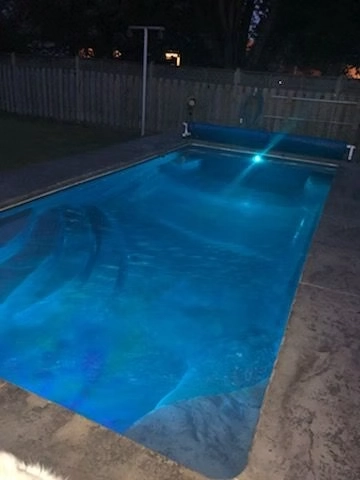 Rectangular in-ground swimming pool illuminated with LED lighting and surrounded by a decorative concrete pool deck.