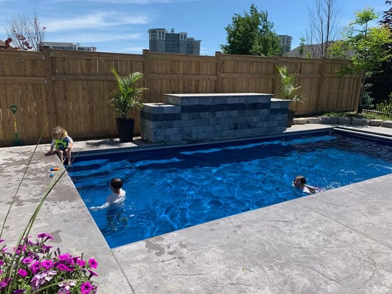 Modern rectangular in-ground swimming pool with decorative concrete patio and contemporary stone water feature.
