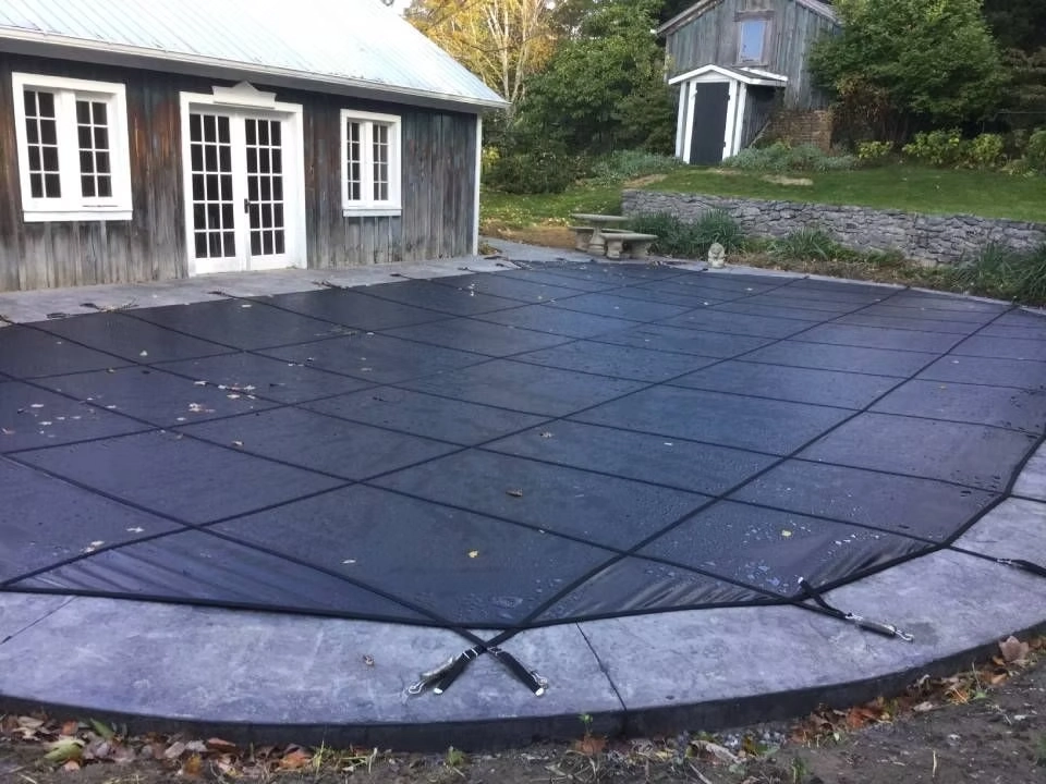 Custom in-ground swimming pool protected with a black mesh safety cover and surrounded by a decorative concrete pool deck.