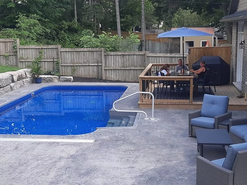 Custom rectangular swimming pool with built-in entry steps, stamped concrete pool deck, and spacious backyard deck.
