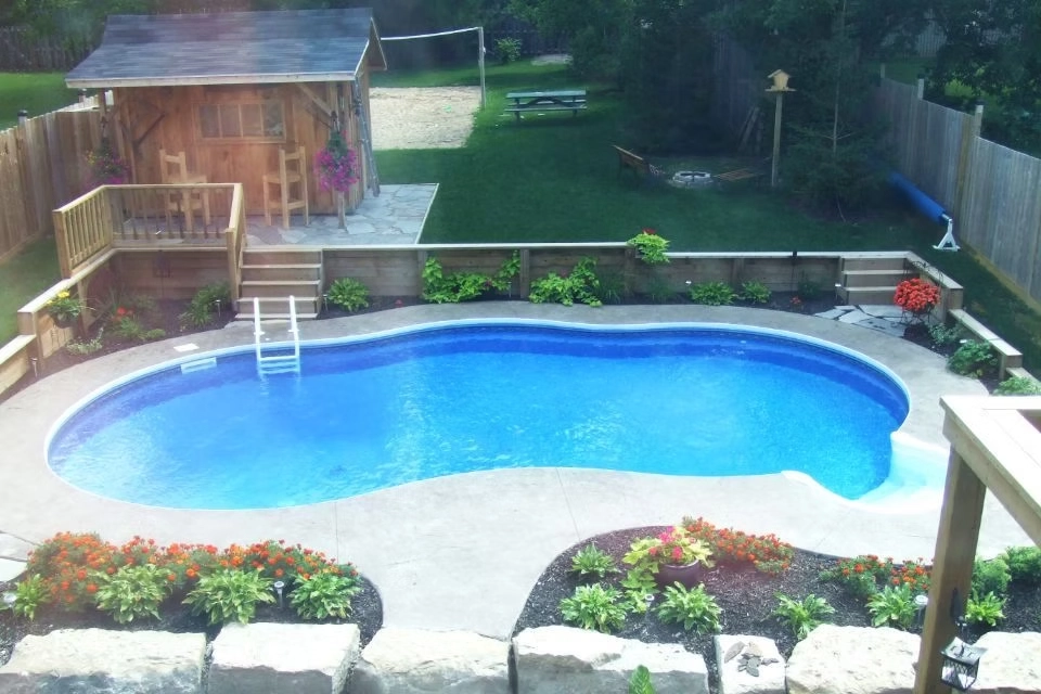 Freeform backyard swimming pool with decorative concrete patio, poolside cabana, and landscaped garden.
