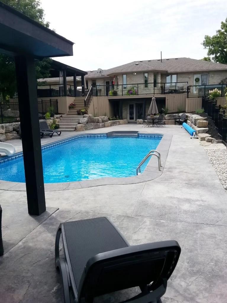 Large custom inground swimming pool with an expansive stamped concrete patio, natural stone retaining walls, and multi-level elevated deck