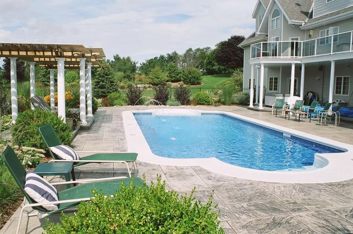 Luxury backyard swimming pool with stamped concrete patio, pergola, and landscaped outdoor living space.