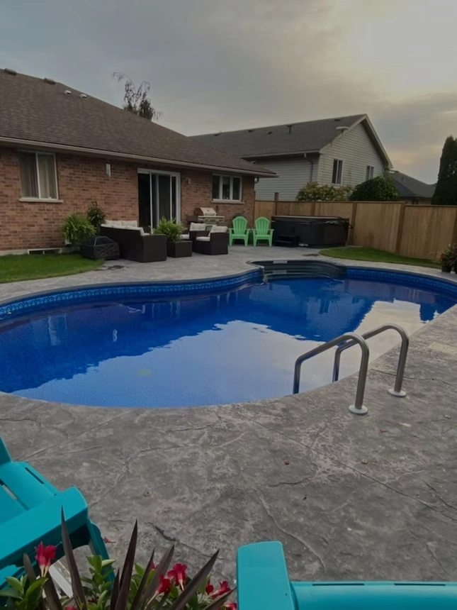 Freeform in-ground swimming pool with stamped concrete patio, backyard seating area, and residential landscape.